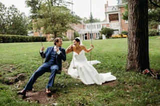 Bride and groom sitting in a charming old swing set in front of the Oneida Community Mansion House